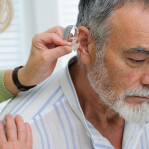 Doctor inserting hearing aid in retiree's ear